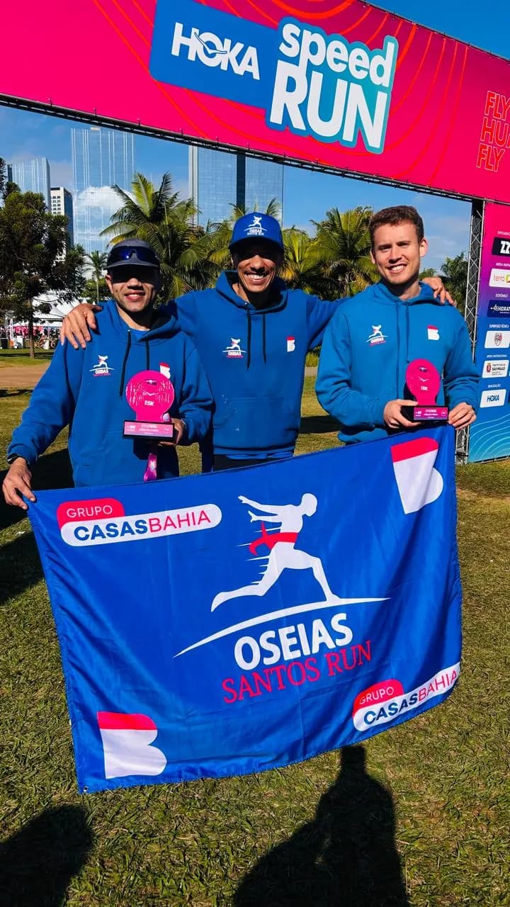 Três atletas da Oseias Santos Run no pódio da Hoka Speed Run com a bandeira da equipe